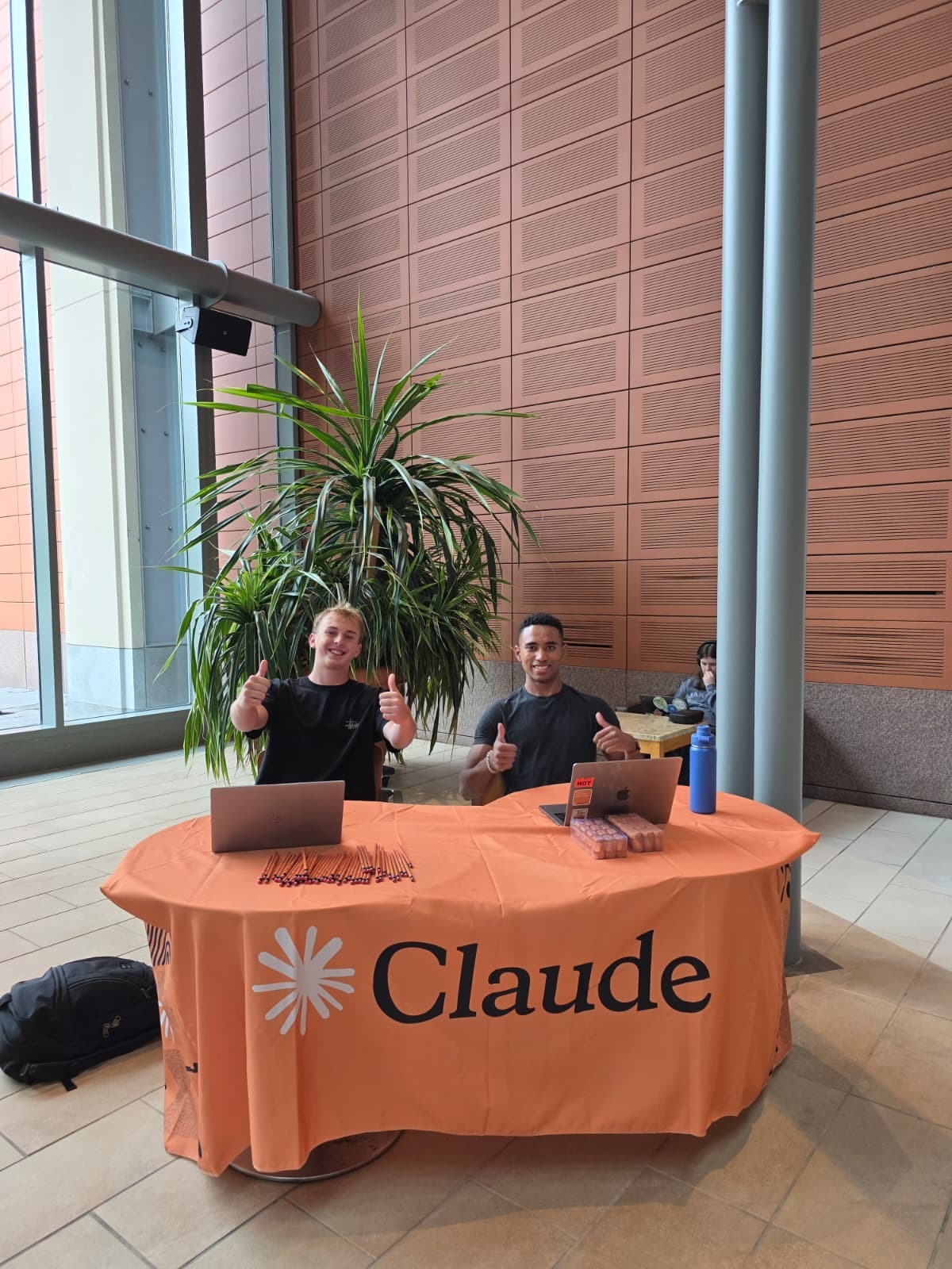 Two students at an orange Claude table in a campus atrium.